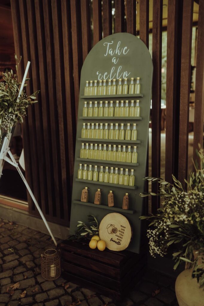 Dunkelgrüne Schautafel mit kleinen Flaschen, Zitronen, Grünzeug und einem Schild mit der Aufschrift Take a Lello.