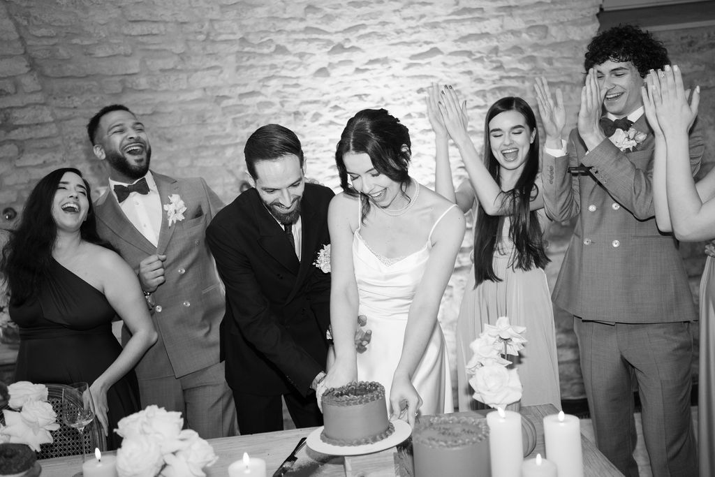 Braut und Bräutigam schneiden eine Torte an, während die Freunde um sie herum lachen und jubeln.
