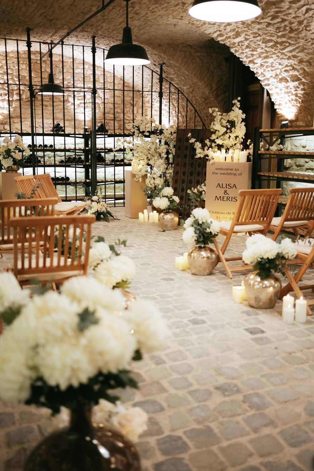 Romantische Hochzeitszeremonie in einem Steinkeller, mit Holzstühlen, weißen Blumen und Kerzen.
