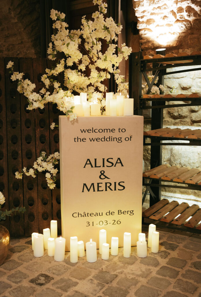 Willkommensschild zur Hochzeit von Alisa und Meris, umgeben von Kerzen und Blumen, datiert 31-03-26.